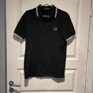 Svart Fred Perry pikétröja L - Klassisk svart pikétröja från Fred Perry med vit logga på bröstet och vita ränder på krage och ärmslut. (Säljer ut kläder just nu så kolla gärna min sida och se om du är intresserad av något mer)