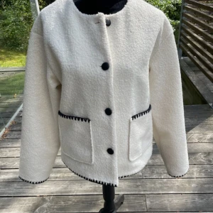 Vit teddyjacka från Vila, stl 36 - Säljer en vit teddyjacka från Vila i storlek 36. Jackan har svarta knappar, två stora fickor framtill och snygga svarta detaljer längs fickor, ärmslut och nederkant. Rak passform och rund halsringning, perfekt för lager-på-lager under höst och vinter. Köpt från jeansbolaget kostade ca 600 nånting. Aldrig använt 