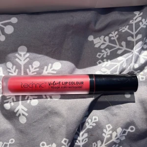 Technic Velvet Lip Colour röd - Flytande läppfärg från Technic i en snygg röd nyans. Velvet Lip Colour ger en matt finish och har en smidig applikator. Perfekt för dig som vill ha intensiva och hållbara läppar. Kommer i en genomskinlig tub med svart lock.