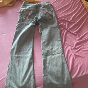 Ljusgrå bootcut jeans från Nelly  - Säljer ett par ljusgrå bootcut jeans från Nelly med slitna hål på knäna och snygga detaljer på bakfickorna. Jeansen har klassisk femficksdesign och är tillverkade i denim. Perfekta för dig som gillar en avslappnad och trendig look. Andvänd en gång 