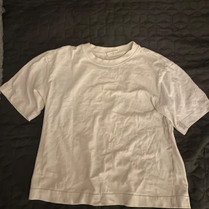 Vit basic t-shirt från Gina Tricot - En klassisk vit t-shirt från Gina Tricot, basically basics-kollektionen. T-shirten har rund hals, korta ärmar och är gjord i mjuk bomull. Perfekt till jeans eller shorts för en clean och enkel look.