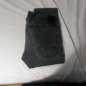 Replay anbass - Säljer ett par svarta Replay anbass jeans med klassisk femficksdesign och snygga detaljer på bakfickorna. Jeansen har en tapered passform som sitter snyggt och är tillverkade i mjukt jeansmaterial. Perfekta för dig som gillar stilrena och bekväma jeans.