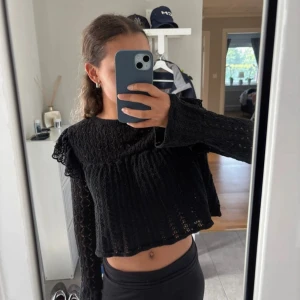 Stickad virkad tröja från Zara - Säljer en svart stickad blus med lång ärm och snyggt stickat mönster. Blusen har volangdetaljer vid axlarna och en knapp i nacken med liten öppning i ryggen. Perfekt för dig som gillar en trendig och chill look.