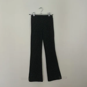 Svarta glittriga leggings från Coccodrillo - Svarta leggings från Coccodrillo med glittriga detaljer som ger en snygg shimmer-effekt. Modellen har utsvängda ben och sitter skönt i midjan. Perfekt för dig som vill sticka ut med lite extra bling i vardagen.