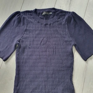 Mörkblå stickad tröja Soaked in Luxury - Supersnygg mörkblå stickad tröja från Soaked in Luxury med puffade ärmar och coolt strukturerat mönster framtill. Rund hals och trekvartsärm ger en chill vibe. Perfekt att styla med jeans eller kjol för en trendig look.