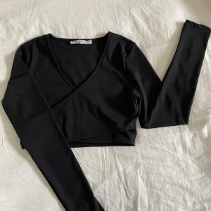 Svart omlottopp från NA-KD - Snygg svart omlottopp från NA-KD i storlek M. Croppad modell med lång ärm och djup v-ringning. Aldrig använd, köpt på åhlens outlet✨