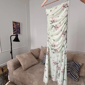 Blommig långklänning från pull and bear - Supersöt långklänning från pull and bear i ljusgrönt med rosa blommor. Klänningen har en axelbandslös design, draperad front och är tillverkad i tunn polyester. Klänningen är superfin och aldrig använd (lappen är kvar) , men säljs då den är lite för liten.