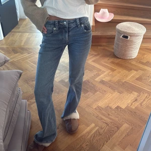 Blå bootcut jeans med låg midja - Säljer ett par blå jeans med bootcut och låg midja. Jeansen har klassisk femficksdesign, snygga detaljer på bakfickan med knapp och är tillverkade i jeansmaterial. Perfekt passform för dig som gillar en avslappnad och trendig look.