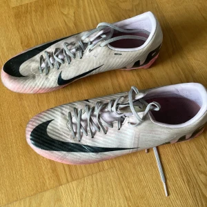 Nike fotbollsskor i ljusrosa och svart - Säljer ett par grymma Nike fotbollsskor i ljusrosa med svarta detaljer och stor Swoosh på sidan. Skorna har snörning och platt sula med dobbar för bra grepp på planen. Lätta och snygga med en sportig vibe, perfekta för dig som vill sticka ut på matchen.