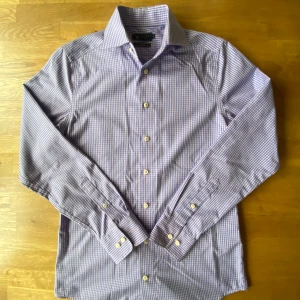 Rutig blå skjorta från Riley Slim Fit - Snygg rutig skjorta från Riley i slim fit-modell, storlek S. Skjortan har ett klassiskt krage, långa ärmar och knappar framtill. Färgen är ljusblå med vita rutor och materialet känns som mjuk bomull. Perfekt för dig som gillar stilrena och fräscha skjortor.