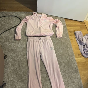 Ljusrosa mjukisbyxor med strassdetalj - Säljer ett par ljusrosa mjukisbyxor från Juicy Couture med glittrande strassdetalj på höften. Byxorna har normal passform, resår och snörning i midjan. Mjukt och skönt material som ger en lyxig känsla, perfekt för chill dagar.