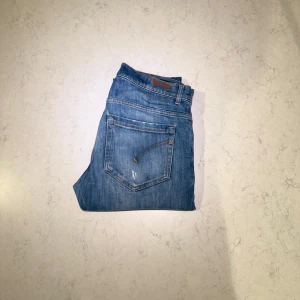 Dondup - Säljer ett par blå Dondup George med snygga slitningar och tvättad look. Jeansen har rak passform, fem fickor och knappgylf. Perfekt för dig som gillar en avslappnad och tidlös stil. Levi's-logga på bakfickan och detaljer i orange.- OBS! Slitningarna var från köp.-Nypris: 2 999 SEK