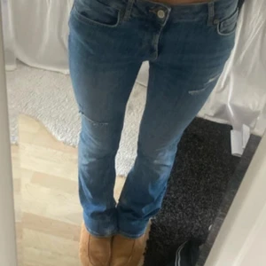 Blå bootcut jeans från Zara - Säljer ett par klassiska blå jeans från Zara med bootcut passform. Jeansen har låg midja, slitna detaljer och lätt tvättad look. I referens är jag 170cm och de gör hela vägen ned