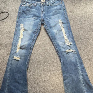 Blå bootcut jeans från True Religion - Säljer ett par blå jeans från True Religion med bootcut passform och slitna detaljer på benen.                                         Midjemått:37 cm   Inerbensmått:78 cm.  Midjehöjd:19 cm skriv gärna prisförslag!!!!!!!!! ordinarie pris 2229