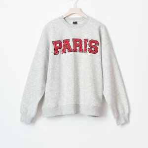 Grå sweatshirt med Paris-tryck - Säljer en grå sweatshirt med stort rött Paris-tryck på bröstet. Tröjan har rund hals, ribbade muddar och är långärmad. Perfekt för dig som gillar streetstyle och vill ha en chill vibe. Passar lika bra till jeans som till mjukisbyxor.