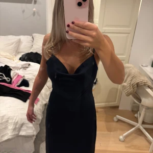 Marinblå långklänning från VILA - Snygg marinblå långklänning från VILA med smala axelband och djup v-ringning. Klänningen har en öppen rygg och är figurnära med slät yta. Materialet är mjukt och känns lyxigt. Dragkedja i sidan för enkel påklädning. Perfekt för dig som vill ha en elegant look.