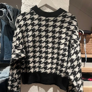 Svartvit stickad tröja med hundtandsmönster - Säljer en svartvit stickad tröja med klassiskt hundtandsmönster. Tröjan har rund hals, ribbade muddar och lång ärm. 