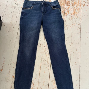 Mörkblå jeans från Mos Mosh - Snygga mörkblå jeans från Mos Mosh med raka ben och klassisk femficksdesign. Jeansen har dekorativa detaljer med nitar vid fickorna fram och broderad logga på insidan av linningen. Perfekt för dig som gillar stilrena och coola jeans.