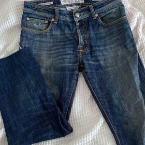 Blå jeans från Jacob Cohen - Snygga blå jeans från Jacob Cohen med klassisk femficksdesign och ljusare tvättade detaljer. Jeansen har raka ben, kontrastsömmar och en brun patch med logga bak. Materialet är lyxigt denim och passformen är normal. Perfekt för dig som gillar stilrena och tidlösa jeans.