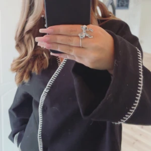 Svart kofta från Gina Tricot med vit kant - Svart kofta från Gina Tricot med kontrasterande vit söm längs kanterna. Koftan har en loose passform, långärmade ärmar och v-ringad hals.