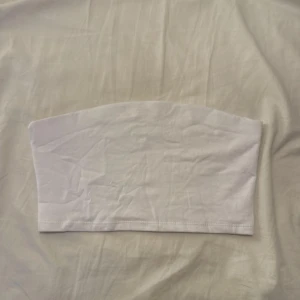 Vit bandeau tubtopp - En enkel och stilren vit bandeau tubtopp i mjuk bomull. Toppen är ärmlös och har en rak, clean design som passar perfekt till sommarens outfits. Snygg att matcha med jeans eller kjol för en chill look.