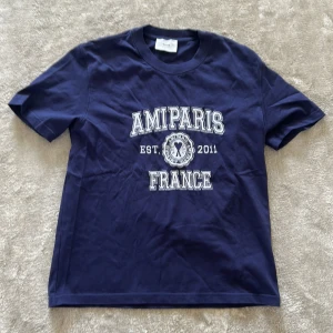 t-shirt från Ami Paris - Snygg mörkblå t-shirt från Ami Paris med vit tryckt text, storlek S och är i fint skick, bara använt ett fåtal gånger. Skriv om du har några frågor