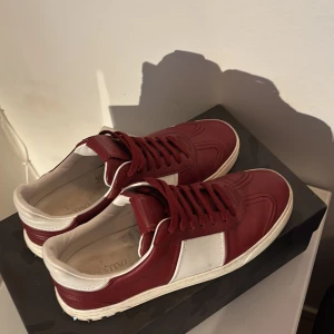 Valentino flycrews. - Valentino Flycrews sneakers i vinrött och vitt skinn med klassiska nitar på hälen. Skorna har rund tå, platt sula och bred vit panel på sidan. Perfekt för dig som vill sticka ut med en lyxig och cool look. Kommer med originalkartong och dustbag. Skriv om ni har några funderingar! Priset är inte huggit i sten! Endast 2 nitar borta
