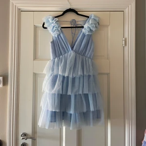 Ljusblå volangklänning från Showpo - Superfin ljusblå kortklänning från Showpo med flera lager volanger och v-ringad omlottfront. Klänningen har breda axelband med rufflade detaljer och knyt i ryggen. 