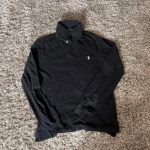 Svart långärmadpikétröja från Polo Ralph Lauren - Svart långärmad pikétröja från Polo Ralph Lauren i slim fit. Är i storlek M men passar mycket mer åt S hållet 🤩🙌
