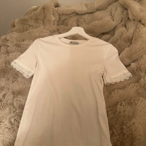Vit topp med spetsdetaljer från Zara - Säljer en vit topp från Zara med korta ärmar och snygga spetsdetaljer vid ärmsluten. Modellen är slim och har en rund halsringning. Perfekt för dig som gillar stilrena plagg med en liten twist. Materialet är mjuk bomull som känns skönt mot huden. Pris kan diskuteras💘💘