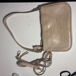 Beige axelväska med krokopräglat mönster - Snygg beige axelväska med krokopräglat mönster och justerbar rem. Väskan har en dragkedja upptill och ett rymligt fack med innerficka. Perfekt storlek för mobil, plånbok och småsaker. Ger en clean och trendig vibe till din outfit. Kommer med justerbart band! Mycket bra Alvin och kvalité!
