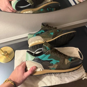 Valentino Rockrunner sneakers camouflage - Säljer ett par Valentino Rockrunner sneakers med grön och turkos camouflage-mönster, svarta och beige detaljer samt ikoniska nitar vid hälen. Väldigt schysst skick och dustbag följer med. Öppen för byten, möts upp på Östermalm eller fraktar.