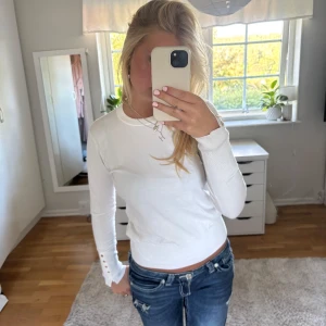 Vit långärmad tröja med knappar - Snygg vit långärmad tröja med rund hals och dekorativa guldfärgade knappar vid ärmsluten. Tröjan öt knappast använd och har inga defekter💕