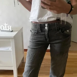 Grå bootcut jeans med dubbla knappar - Snygga grå jeans med bootcut passform och dubbla knappar i midjan. Jeansen har klassiska fem fickor och cool tvättad look. Perfekta för dig som gillar en avslappnad men trendig stil.
