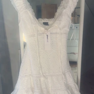 Vit spetsklänning från Gina Tricot - Supersöt vit klänning från Gina Tricot med spetsdetaljer och volanger. Klänningen har ärmlös design med breda axelband och v-ringad hals. Perfekt för sommarens alla tillfällen, och den har en romantisk och fräsch look.