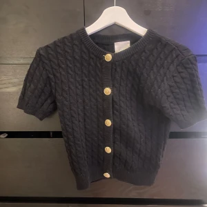 Svart kabelstickad kofta från H&M - Svart kabelstickad kofta från H&M med korta ärmar och snygga guldknappar framtill. 🌸