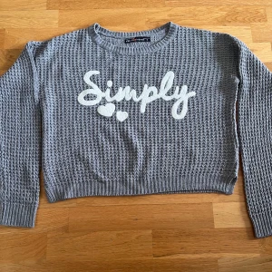 Grå stickad tröja från FB Sister - Säljer en grå stickad tröja från FB Sister med texten 'Simply' och två hjärtan i vitt framtill.