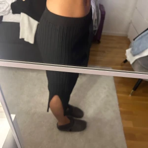 Svart ribbad kjol med slits - Säljer en svart ribbad kjol i midilängd med hög midja och slits på sidan. Kjolen har en kroppsnära passform och är superenkel att styla till olika looks. Perfekt för dig som gillar stilrena plagg med en twist.