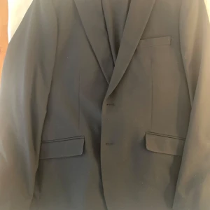 Svart kostym från Hampton Republic - Säljer en klassisk mörkblå kostym från Hampton Republic i storlek 52. Kavajen har två knappar, bröstficka och två fickor med lock. Perfekt för formella tillfällen och stilrena outfits.