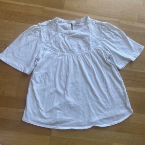 Vit blus med broderi från Zara - Säljer en söt vit blus från Zara med broderade detaljer och korta ärmar. Blusen har en lös passform och fina spetsinslag upptill. Perfekt för vår och sommar!