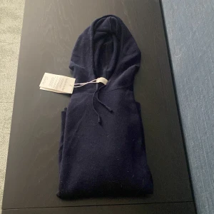 Mörkblå kashmirtröja med huva från Sayless -  mörkblå tröja i kashmir från Sayless med huva. Tröjan har lång ärm och en enkel, stilren design som passar perfekt till vardags. Superskön och lyxig känsla tack vare det mjuka materialet.Helt ny, aldrig använd 