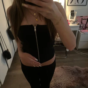 Svart tubtopp med dragkedja - Säljer en svart tubtopp med dragkedja framtill. Toppen är tight och axelbandslös. Den är i M men den är väldigt stretchig jag brukar ha xs-s.