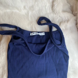 Mörkblå ribbad linnetopp från NA-KD - Säljer en mörkblå ribbad linnetopp från NA-KD med smala axelband. Toppen är ärmlös och har en enkel, stilren design som passar perfekt till sommaren. Superfin att matcha med jeans eller kjol!