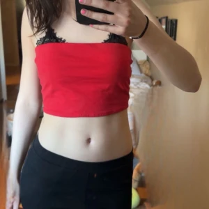 Röd croppad tubtopp - Säljer en röd croppad tubtopp med svarta spetsdetaljer upptill. Perfekt för sommardagar eller när du vill ha en enkel men snygg look. Toppens material känns mjukt och stretchigt.