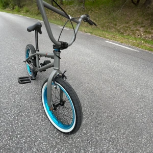 Grå BMX-cykel från Wicked Family - Säljer en grå BMX-cykel från Wicked Family med svarta detaljer och blå fälgar. Cykeln har robust ram, svarta handtag och sadel samt vita däcksidor. Perfekt för tricks och street riding. Den är relativt sliten men funkar utmärkt.         Kan hämtas i Skåne.                                               Hör av dig om du är intresserad.          