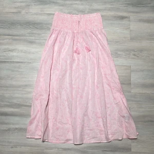 Mönstrad ljusrosa  långkjol från Gina Tricot - Supersöt mönstrad ljusrosa långkjol från Gina Tricot med smock i midjan och knytband med tofsar. Kjolen har ett diskret mönster och är tillverkad i ett lätt och luftigt material, perfekt för varma dagar. 