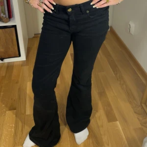 Svarta bootcut jeans från Louis - Säljer ett par svarta bootcut jeans med låg midja och klassisk femficksdesign. Jeansen har knapp- och dragkedjestängning framtill och är i ett mjukt denimtyg. Perfekta för dig som gillar en retroinspirerad look.