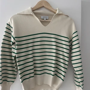 Vit och grön randig stickad tröja från Other stories  - Säljer en krämvit stickad tröja med gröna horisontella ränder från Other stories. Tröjan har en v-ringning med krage och långa ärmar. Perfekt för en stilren och avslappnad look.