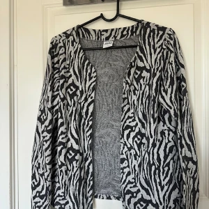 Zebramönstrad cardigan jacka från vero Moda - Säljer en svartvit cardigan jacka från Mixed med zebramönster. Jackan har lång ärm och öppen front utan knäppning. Perfekt för att addera lite edge till din outfit.