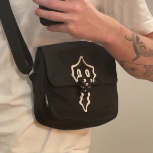 Trapstar väska - Säljer en svart axelväska från Trapstar med justerbar rem och ett unikt vitt emblem på locket |Säljer då jag inte använder den.                               | Knappt använd | ❕Tveka inte på att höra av dig vid intresse 
